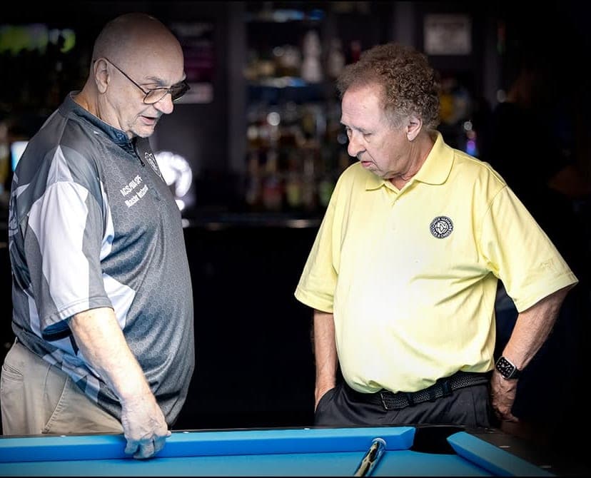 Randy Goettlicher talking a student through a shot at the table, wearing his ACS Hall of Fame Master Instructor jersey.